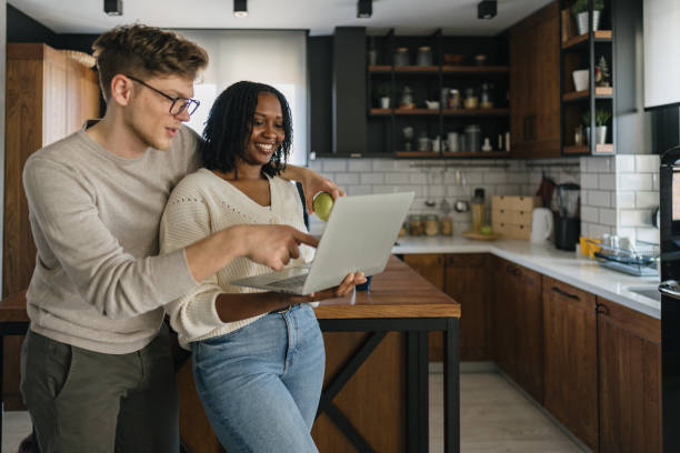 Young couple using laptop in kitchen looking at recipes
