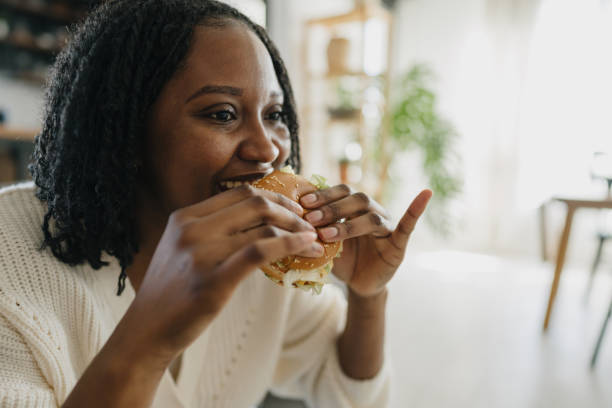istock Young woman enjoying eating a hamburger at home 2198884890