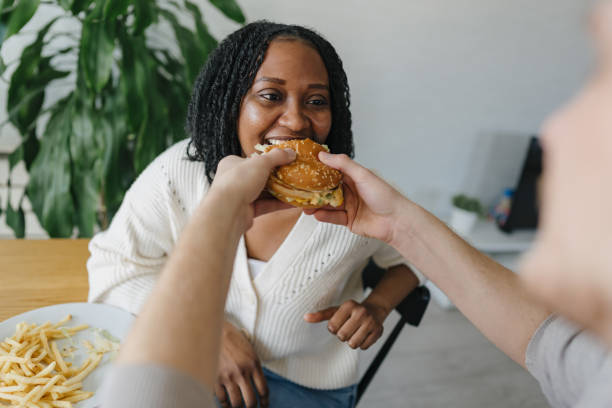 istock Woman taking a big bite of a burger offered by her partner 2198884997