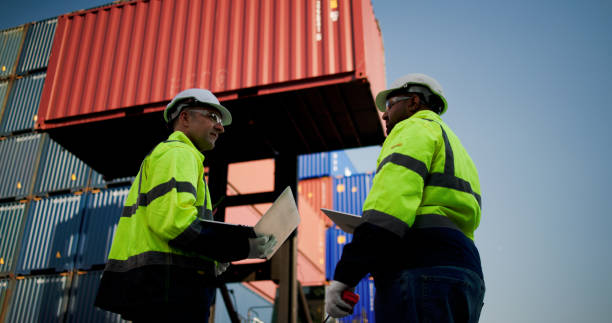 istock Logistic engineers and workers with a bright green safety jacket and safety PPE working at the container shipping yard 2198895921