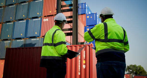 istock Logistic engineers and workers with a bright green safety jacket and safety PPE working at the container shipping yard 2198895923