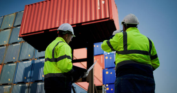 istock Logistic engineers and workers with a bright green safety jacket and safety PPE working at the container shipping yard 2198895924
