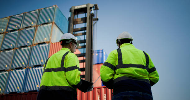 istock Logistic engineers and workers with a bright green safety jacket and safety PPE working at the container shipping yard 2198895944