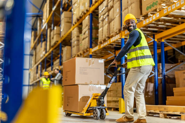 istock Warehouse Worker Operating a Pallet Jack with Stacked Boxes and Shelves 2198896409