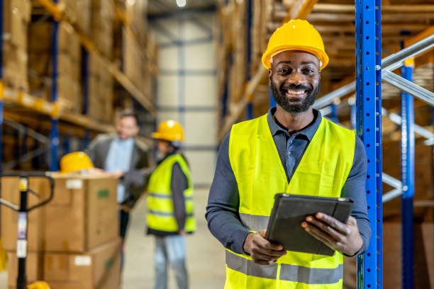 istock Warehouse Worker Smiling in Safety Gear with Colleagues in Industrial Setting 2198897705