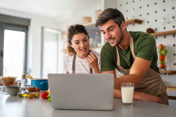 istock Young couple using laptop computer to take part in online culinary workshop, cooking together 2198897914