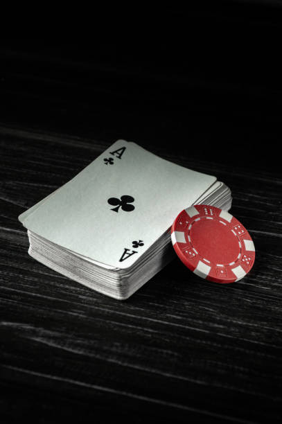 A stack of playing cards sits beside a red poker chip, illuminated softly in a darkened room, reflecting the thrill and tension of a high-stakes casino atmosphere