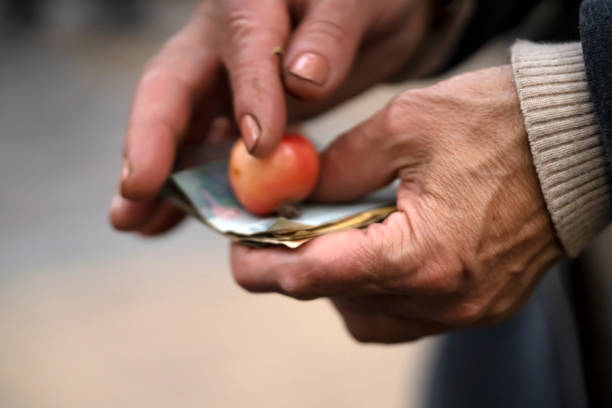Hands with wrinkles hold banknotes and an apple, close-up view. Concept in dark colors on the theme of poverty, economic and food crisis, hard poor life of people.