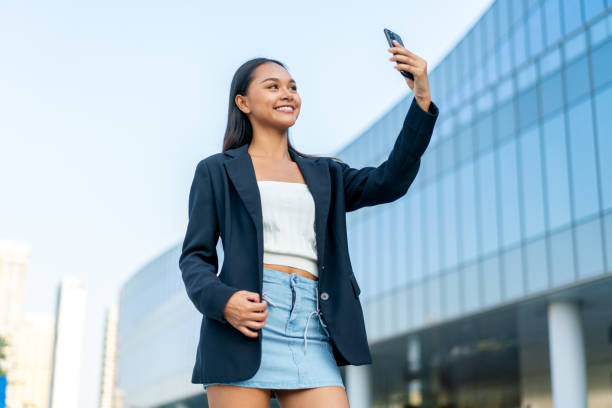 istock Young Woman Using Phone in Front of Modern Glass Office Building 2198902974