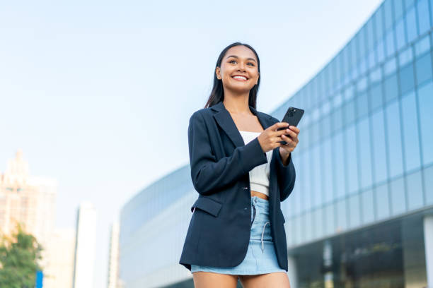 istock Young Woman Using Phone in Front of Modern Glass Office Building 2198903140