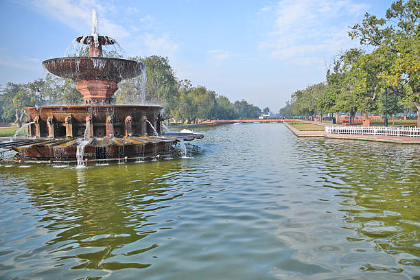 A majestic fountain with cascading water in a large pond, framed by trees and a peaceful park setting.