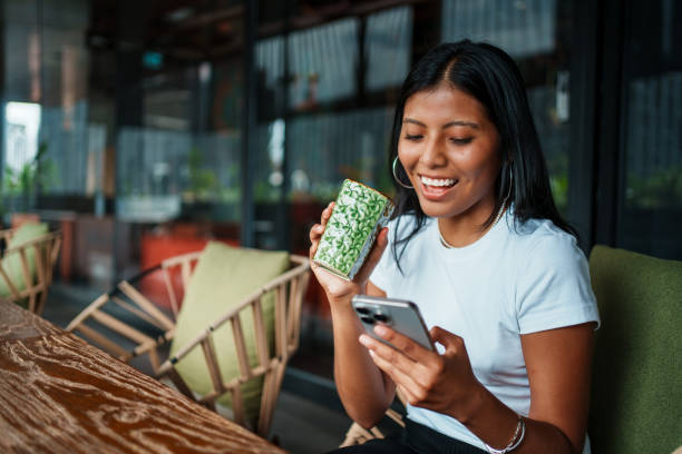 istock A Smiling Woman Delightedly Enjoying a Refreshing Drink and Using Her Phone in a Modern Cafe Setting 2198906742