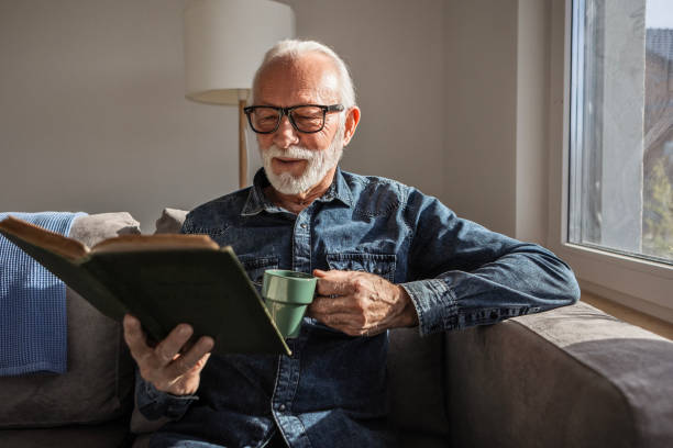 istock Senior man is reading book with a cup of coffee 2198909822