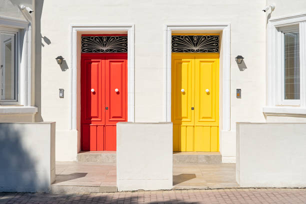 istock Red and yellow door side by side on white building facade, basking in sunlight. 2198912576