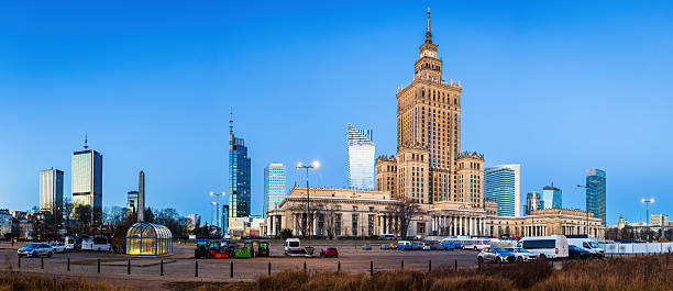 Early morning in Warsaw. The first sunlight illuminates the Palace of Culture and Science, casting a golden glow on its historic facade. Modern skyscrapers rise behind, contrasting past and present.