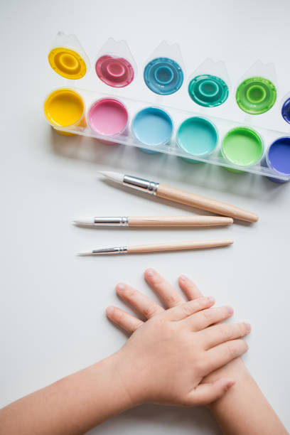 istock Childs hands with watercolor paints and brushes on a white surface 2198915263