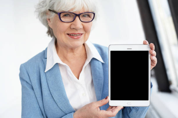 istock Electronic devices, gadgets, technology and connection concept. Joyful elegant elderly European gray haired woman in eyewear presenting digital tablet with black display with copyspace for your text 2198915947