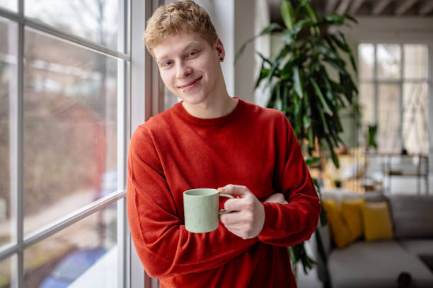 istock Young man enjoying a warm beverage in a cozy home setting while relaxing by the window 2198918046