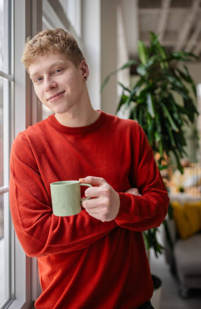 istock Young man in a cozy home setting enjoying a cup of coffee while posing by the window 2198918333