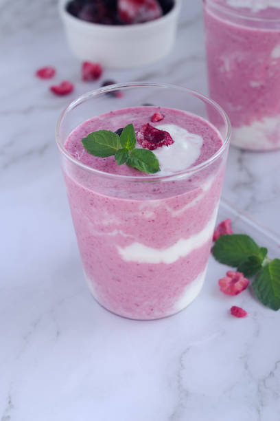 a glass of homemade mixed berry yogurt smoothie decorating with fresh mint leaves on marble table background.