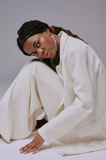 istock Kneeling Woman Posing in White Suit Against Neutral Background 2198921438