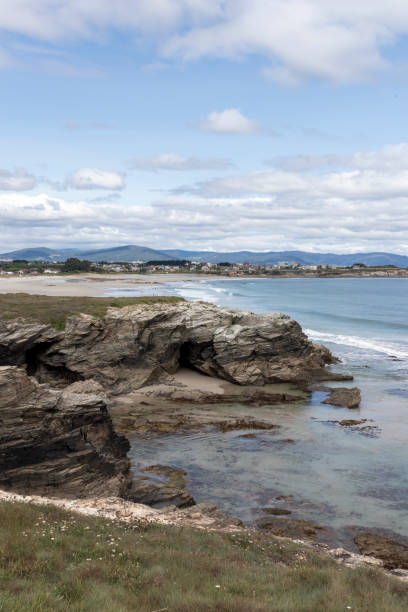 istock Scenic coastal landscape with rocky cliffs, sandy beaches, crystal-clear water, and distant town under a partly cloudy sky. Peaceful and picturesque seashore 2198924987