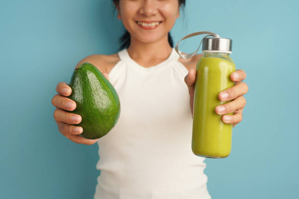 istock Close up Woman holding avocado fruit and juice on light blue background 2198930816