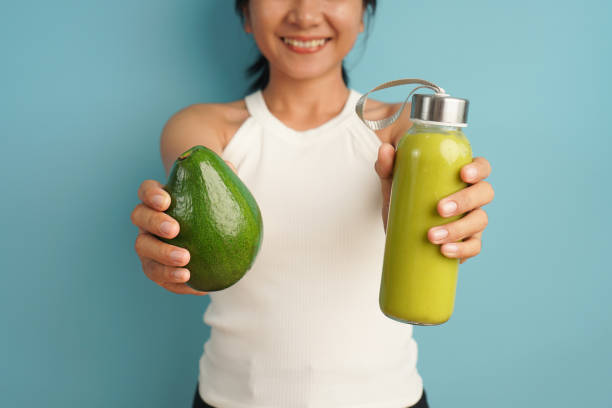 istock Woman holding avocado fruit and smoothie on light blue background 2198930846