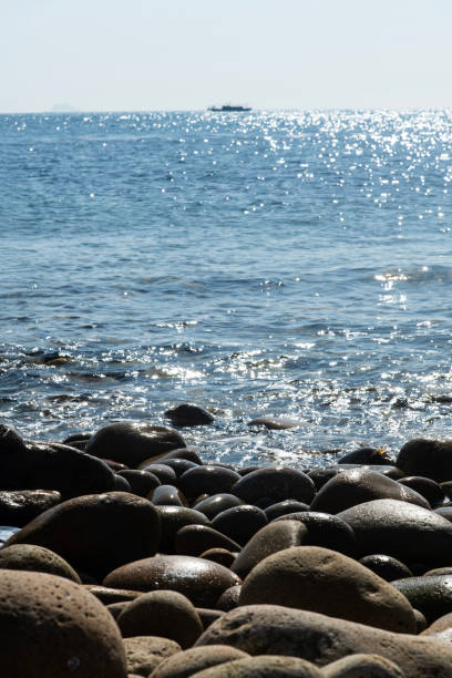 The blue wave rolls onto a  round pebbles  beach in the white rays of  sun.