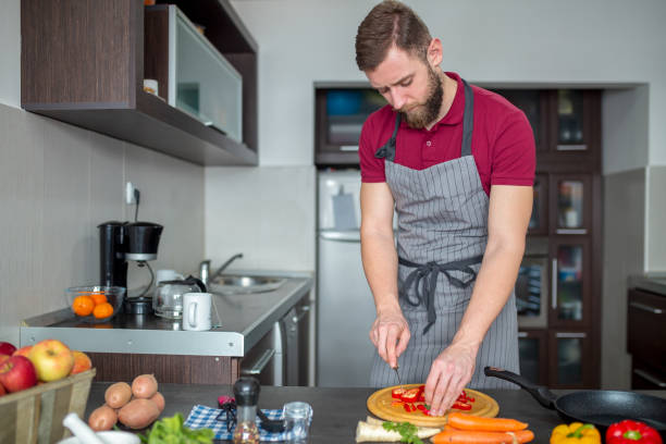 istock Man cuts fresh spring vegetables on the kitchen table, closeup. Preparing homemade food, home kitchen interior. 2198935977