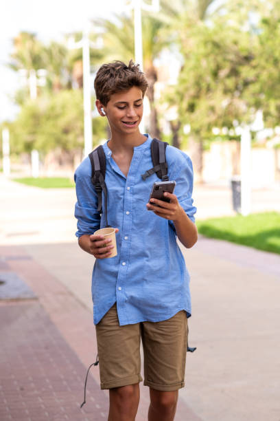 istock Teenager student with backpack and a drink to carry uses his smartphone while strolling through a residential area. 2198943166