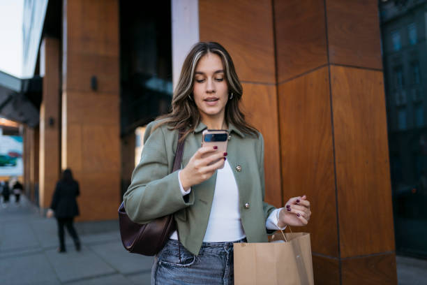 istock Young woman using smartphone while carrying shopping bag in city 2198943830