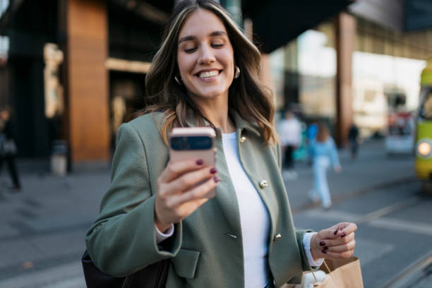 istock Smiling young woman using smartphone while walking in the city 2198944091