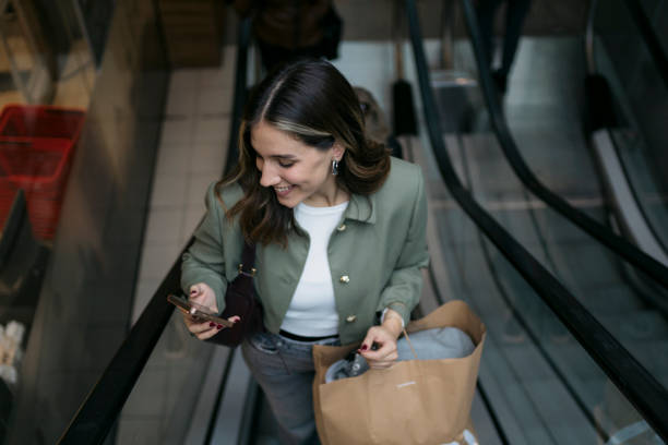 istock Smiling woman using smartphone on escalator holding zara shopping bag 2198944787