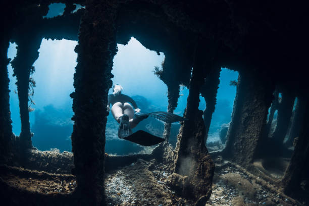 istock Freediver explores underwater shipwreck, surrounded by light rays and marine growth. Free diving at wreck ship 2198951826