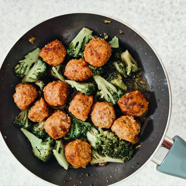 The photo depicts a hot pan in which there are ruddy meat balls with a crispy crust. Their surface is slightly caramelized, toasted sides shine with natural juices, and spices form a fragrant crust. Bright green broccoli blossoms are located between the meat balls. The bright light of the lamp highlights the mouth-watering shine of the oil and the texture of each ingredient. This image conveys the taste of life – the comfort of home, the love of cooking and the aesthetics of food, which awakens the appetite even before the first bite.