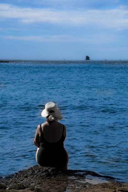 Mature woman sitting on a rock in Culebra Bay on the Pacific Ocean in Costa Rica