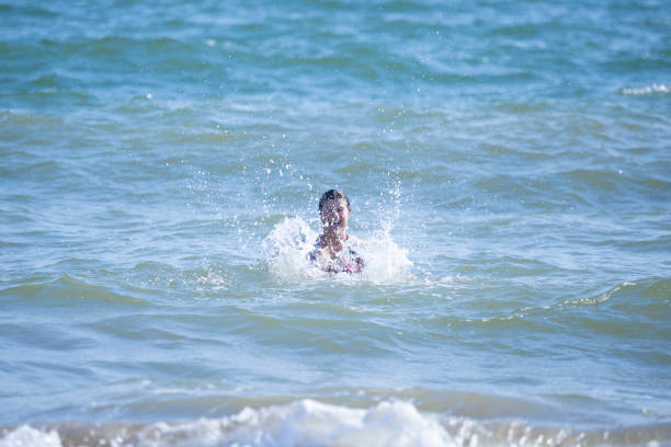 A lively moment of a woman splashing in the waves, enjoying the refreshing ocean at Isla Canela Beach. Perfect for energetic summer vacation themes and travel promotions