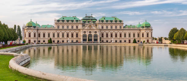 Vienna, Austria - August 31, 2022: The Upper Belvedere Palace reflects gracefully in a curved pond that forms part of its surrounding gardens. The symmetrical design and mirror-like water highlight the elegance of Austrian baroque architecture.