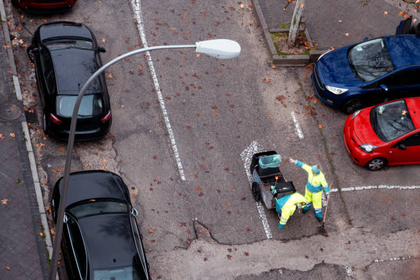 A person belonging to the cleaning service of Madrid, has picked up a piece of paper with her hand and puts it in the garbage can that has wheels and is where the worker carries all the cleaning utensils to do her job.