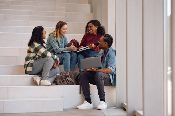 istock Happy university friends talking while relaxing on stairs in a hallway. 2198962228
