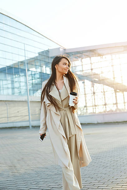 istock Beautiful smiling woman walking on near office from work with coffee cup and texting on mobile phone.Phone communication. 2198962421