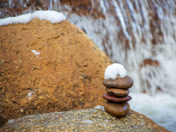 Rock Cairn with Snow and Flowing Waterfall