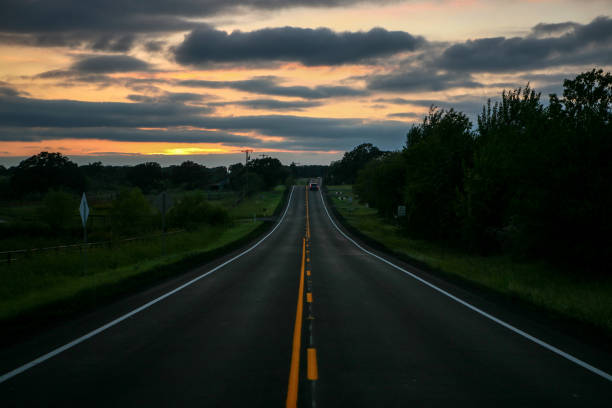 Setting sun on a two-lane blacktop highway in the country with a dramatic sky