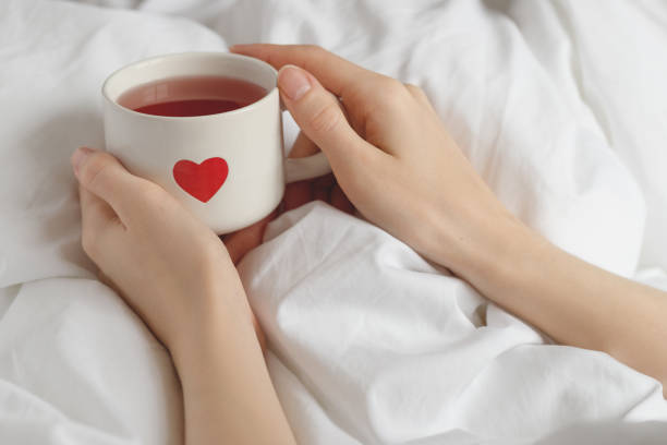 istock Cozy Morning in Bed: Hands Holding a Cup of Tea with a Heart Design. Romantic morning routine 2198971368
