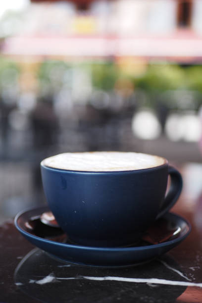 A dark blue cup filled with rich cappuccino sits on a table, accompanied by a blurred background