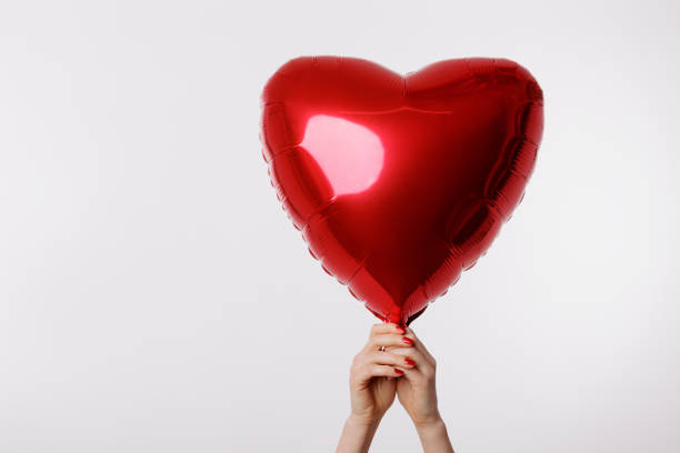 istock A hand holding a shiny red heart-shaped balloon against a clean white background, symbolizing love, romance, and celebration. 2198976212