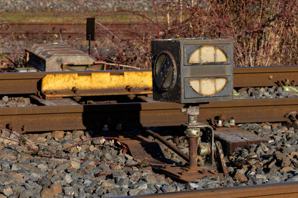 A railway signal control stands prominently beside the tracks, catching the sunlight. Surrounding gravel and track adjustments highlight the importance of safety in train operations during the day.