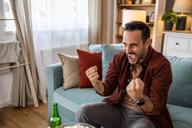 istock Young man cheering while watching sports game on TV 2198983663