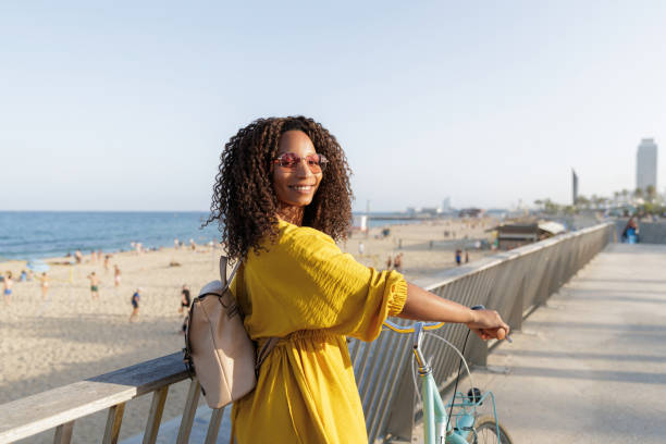 istock Young woman with backpack and sunglasses is holding her bicycle while enjoying summer vacation at beach 2198984590